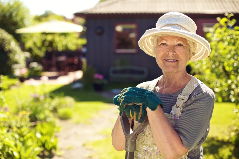 Portrait,Of,Senior,Woman,Wearing,Hat,With,Gardening,Tools,Outdoors.