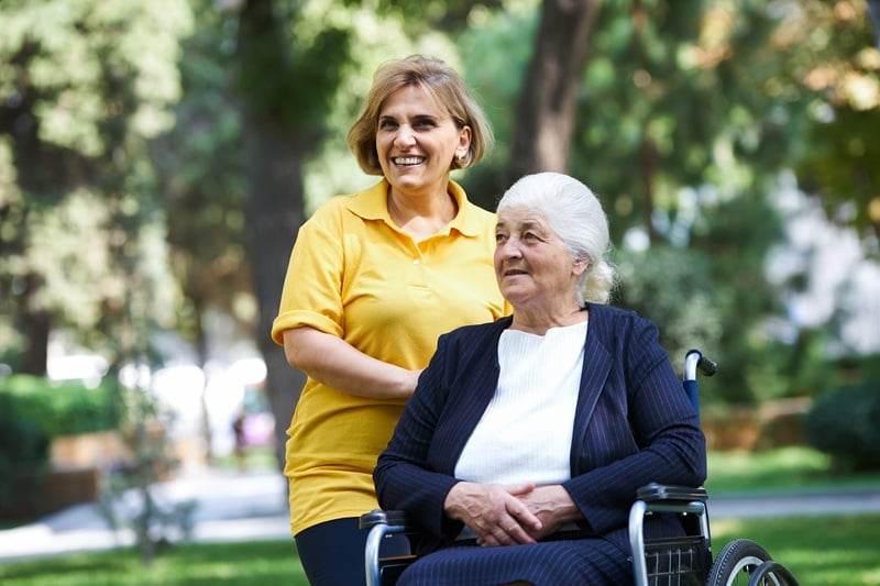 Professional helpful caregiver and handicapped senior woman. Daughter cares for mother. Health visitor and a senior woman during visit. Careful caregiver taking care of the patient, outdoors.
