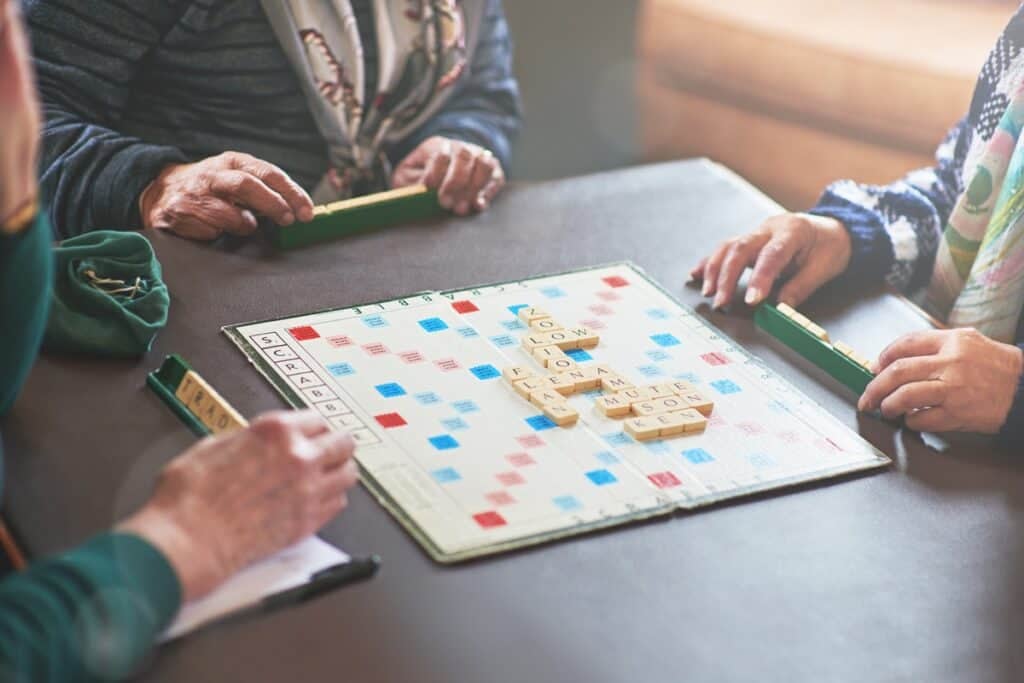 Board game, table and senior people playing in nursing home for retirement and friendly contest. Crossword, puzzle and battle of elderly woman in house winning with strategy, choice and challenge.